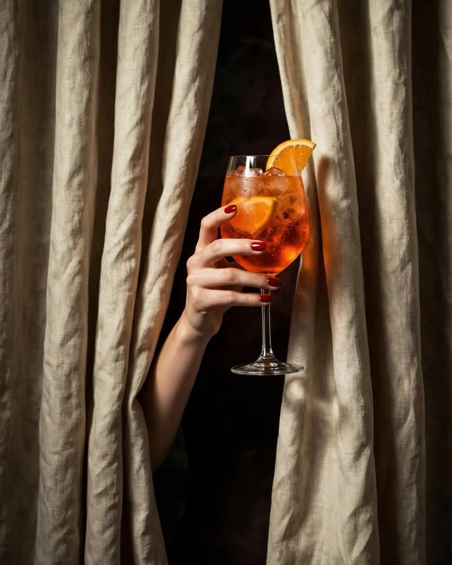 Mano sosteniendo un spritz entre cortinas